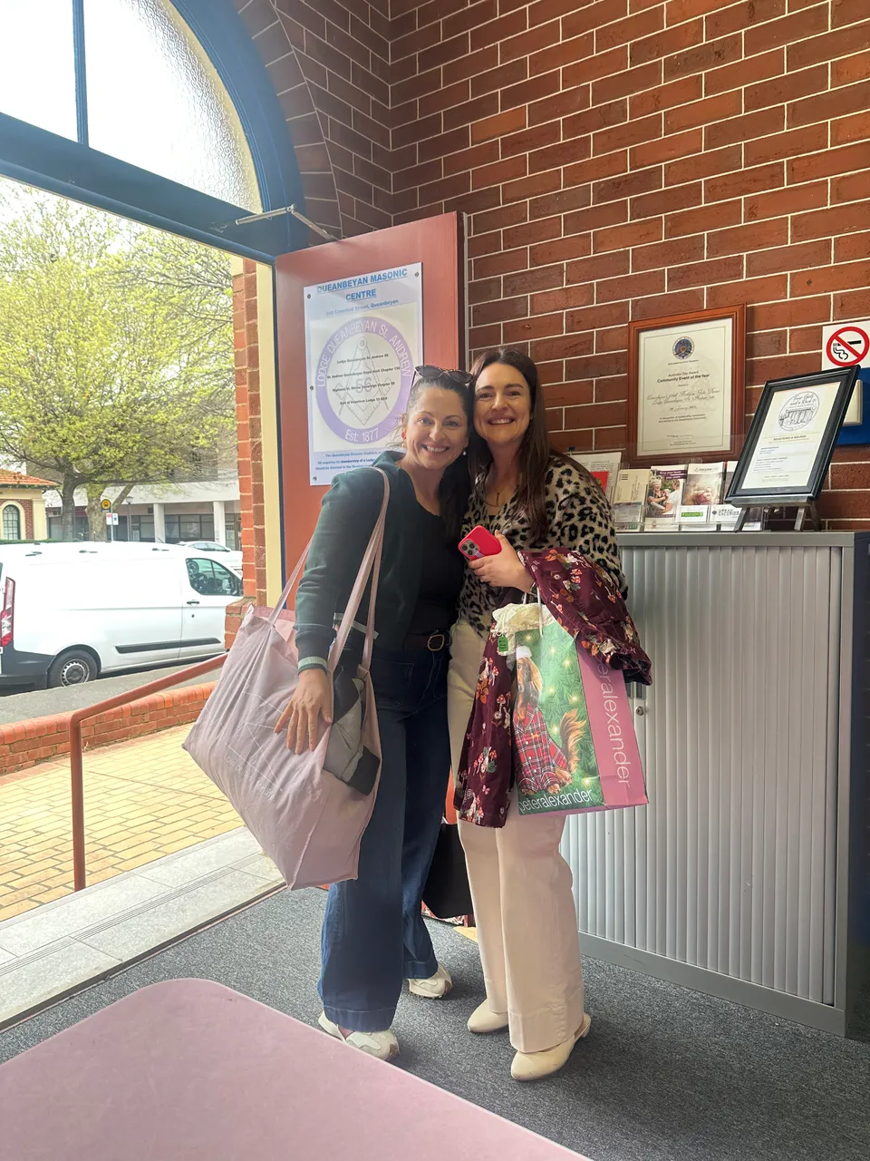 Two smiling shoppers standing together with their shopping bags.