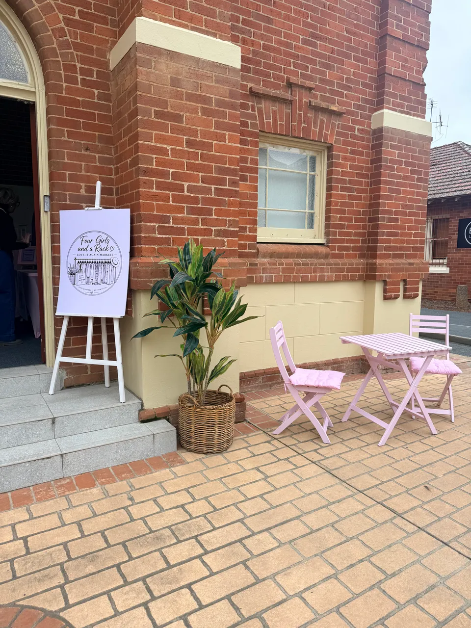 Four Girls and a Rack signage beside plants and pink seating at the market entrance.