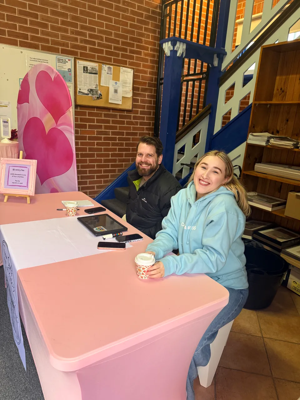 Two people smiling behind the pink market welcome desk.